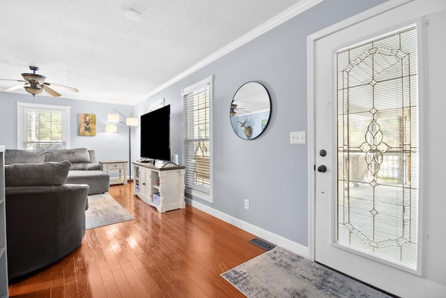 living area with visible vents, ornamental molding, hardwood / wood-style floors, baseboards, and ceiling fan