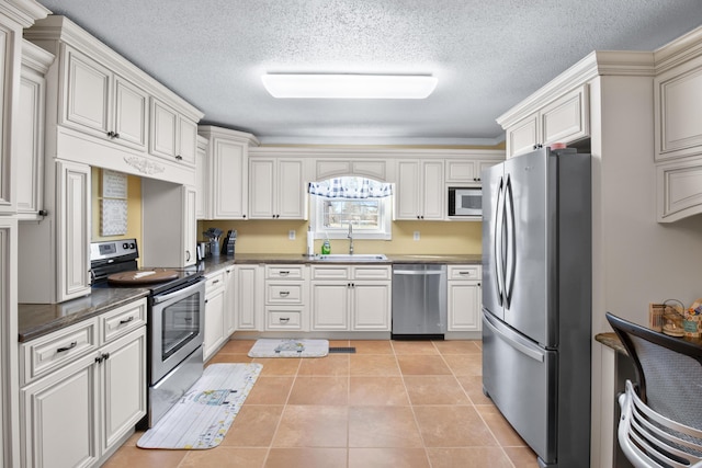 kitchen with a sink, dark countertops, appliances with stainless steel finishes, and light tile patterned floors