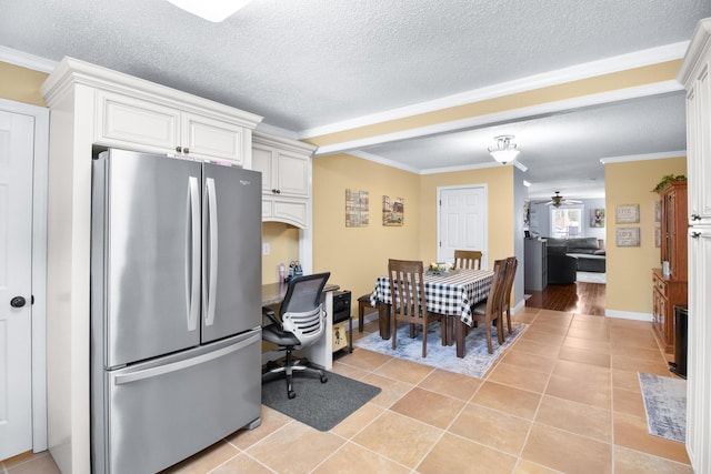 kitchen featuring light tile patterned flooring, freestanding refrigerator, a textured ceiling, white cabinetry, and crown molding