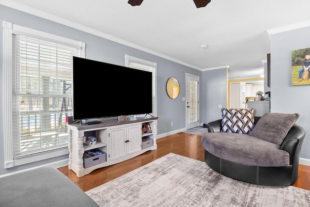 living room with a ceiling fan, crown molding, baseboards, and wood finished floors