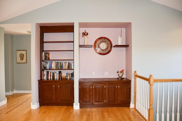 hallway with light hardwood / wood-style floors, lofted ceiling, and built in features