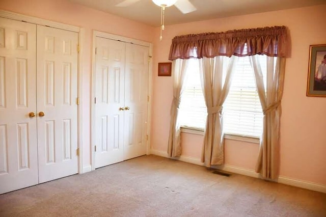 unfurnished bedroom with ceiling fan, light carpet, and multiple closets