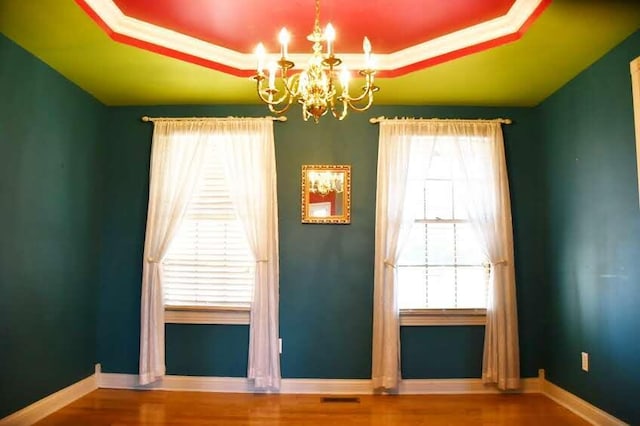 spare room featuring hardwood / wood-style floors, an inviting chandelier, a raised ceiling, and crown molding