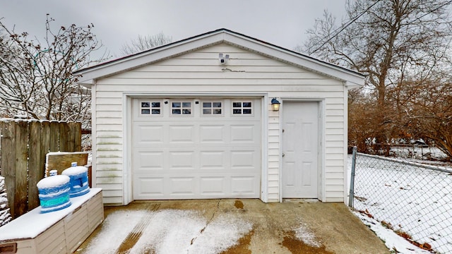 snow covered garage with a garage, fence, and driveway