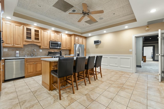 kitchen with appliances with stainless steel finishes, a raised ceiling, a kitchen island, and a breakfast bar area