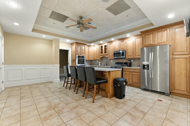 kitchen featuring a breakfast bar area, tasteful backsplash, ornamental molding, a tray ceiling, and stainless steel appliances