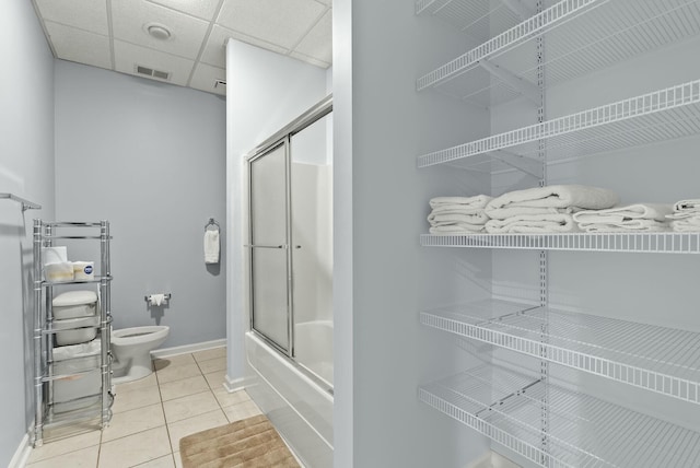 bathroom with tile patterned flooring, a paneled ceiling, shower / bath combination with glass door, and toilet