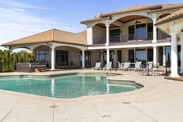 rear view of house featuring ceiling fan, a balcony, a swimming pool with hot tub, and a patio