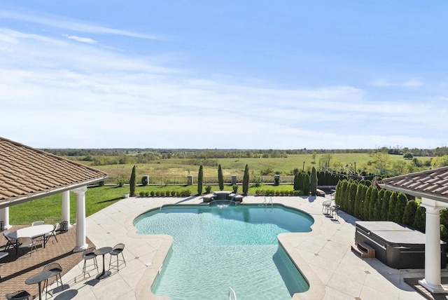 view of swimming pool with a hot tub, a patio, and a rural view