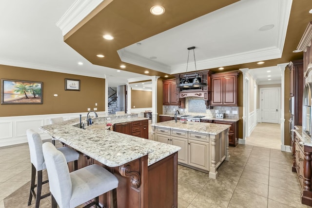 kitchen featuring a spacious island, light tile patterned floors, a raised ceiling, pendant lighting, and light stone countertops