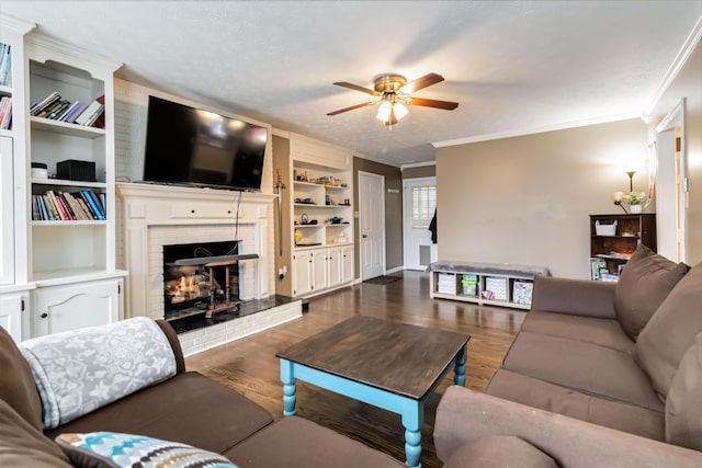 living room with crown molding, a brick fireplace, dark hardwood / wood-style floors, built in features, and ceiling fan