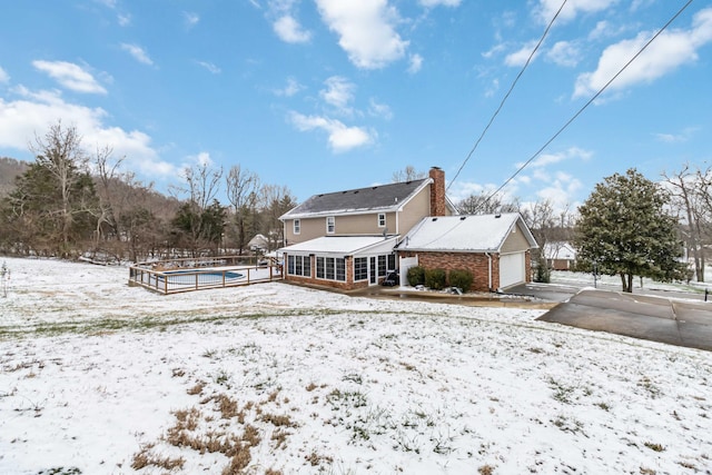 snow covered rear of property featuring a swimming pool and a garage