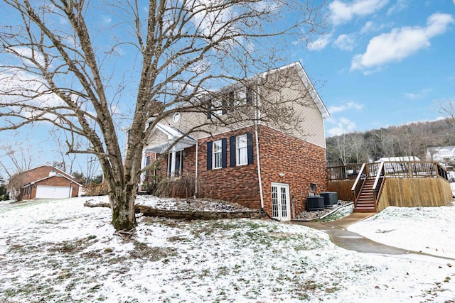 snow covered property with an outbuilding, a garage, central AC unit, and a deck