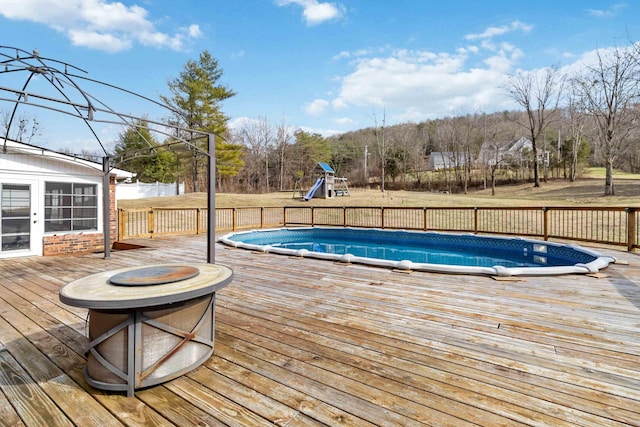 view of pool with a wooden deck, an outdoor fire pit, and a playground