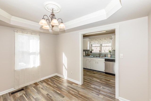 unfurnished dining area featuring hardwood / wood-style floors, a tray ceiling, an inviting chandelier, and sink