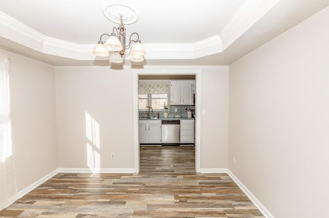 unfurnished dining area with sink, an inviting chandelier, a raised ceiling, light wood-type flooring, and ornamental molding