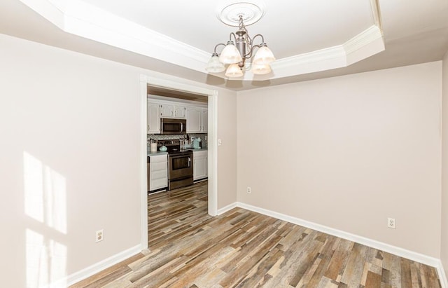 unfurnished dining area featuring a chandelier, light hardwood / wood-style floors, a raised ceiling, and crown molding