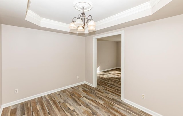 unfurnished dining area featuring a chandelier, hardwood / wood-style floors, a raised ceiling, and ornamental molding