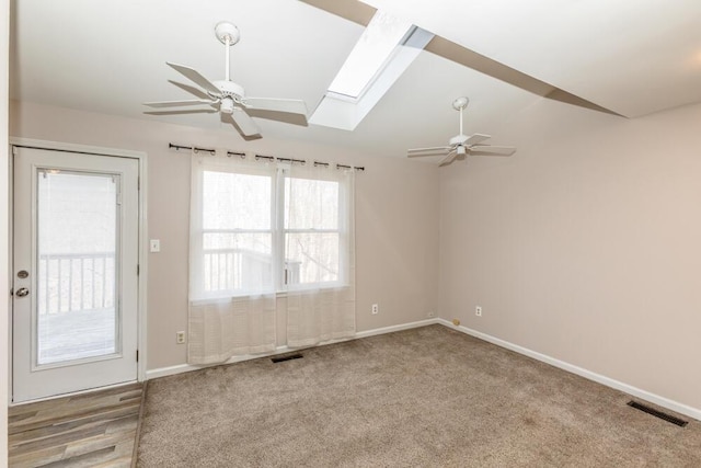 carpeted spare room featuring vaulted ceiling with skylight and ceiling fan