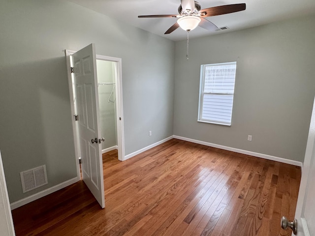 unfurnished bedroom featuring a closet, a walk in closet, ceiling fan, and hardwood / wood-style floors