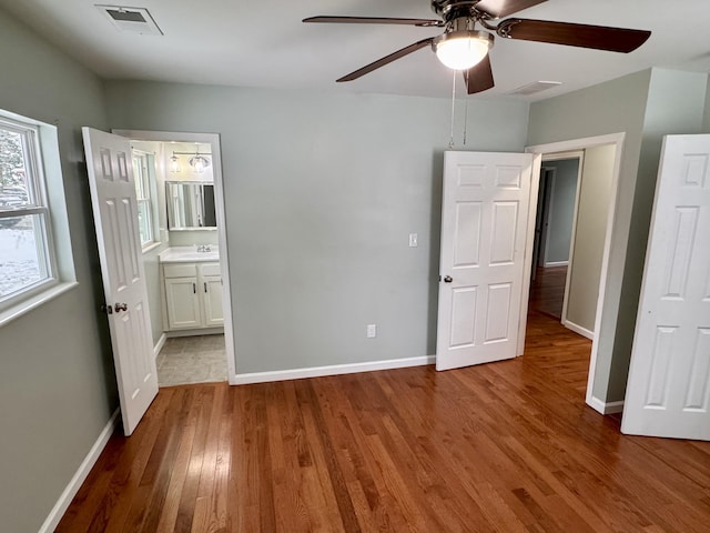 unfurnished bedroom with ceiling fan, sink, wood-type flooring, and ensuite bathroom