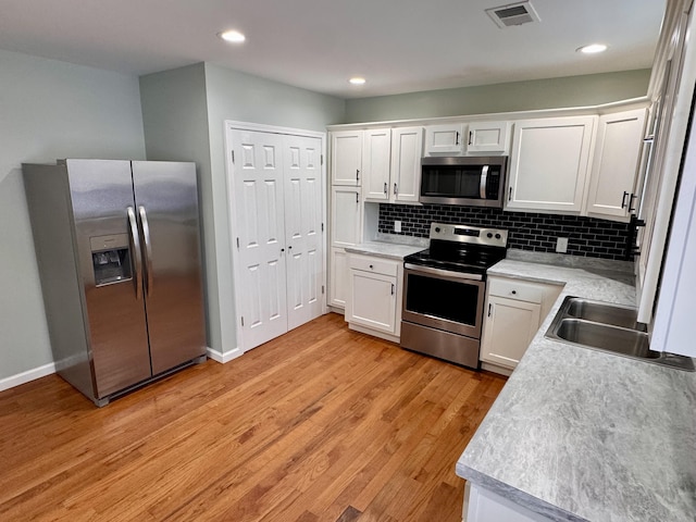 kitchen featuring decorative backsplash, light wood-type flooring, stainless steel appliances, sink, and white cabinets