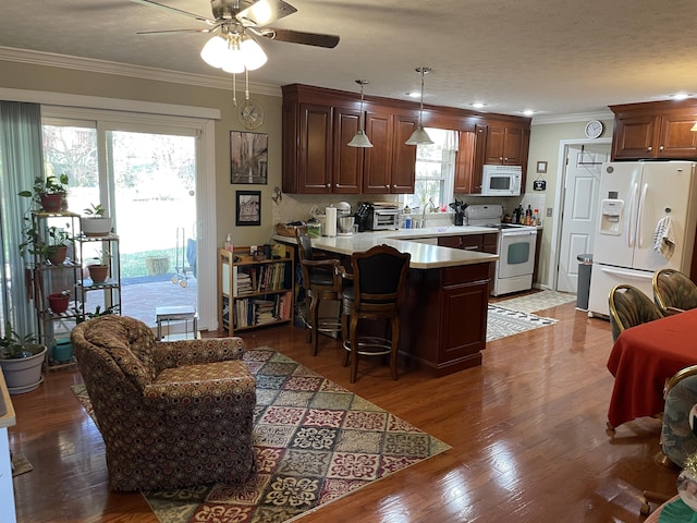 kitchen featuring hanging light fixtures, kitchen peninsula, plenty of natural light, white appliances, and a kitchen bar