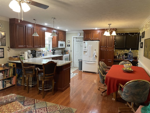 kitchen with kitchen peninsula, crown molding, pendant lighting, and white appliances