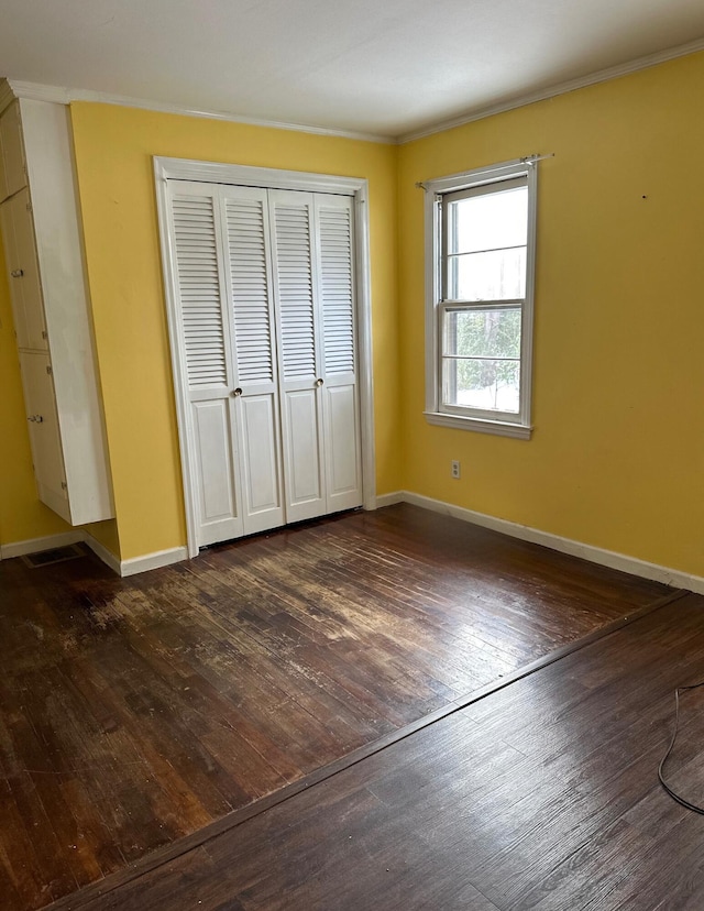 unfurnished bedroom featuring dark hardwood / wood-style flooring, crown molding, and a closet