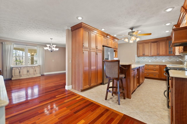 kitchen featuring ceiling fan with notable chandelier, decorative backsplash, decorative light fixtures, a kitchen island, and stainless steel refrigerator