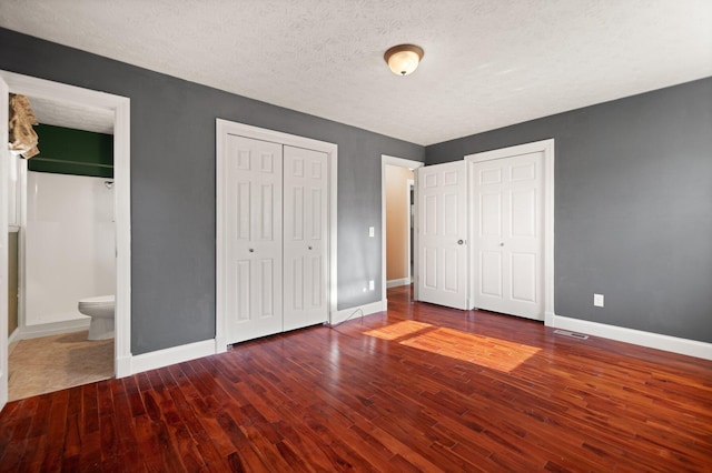 unfurnished bedroom with a textured ceiling, hardwood / wood-style flooring, multiple closets, and ensuite bathroom