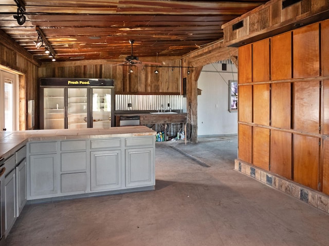 kitchen featuring tile counters, ceiling fan, wood walls, and built in fridge