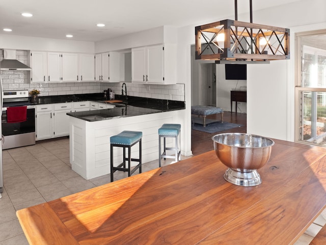 kitchen featuring light tile patterned floors, white cabinetry, stainless steel electric range, wall chimney range hood, and pendant lighting