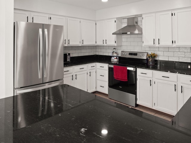 kitchen with white cabinets, appliances with stainless steel finishes, wall chimney range hood, dark stone countertops, and tasteful backsplash