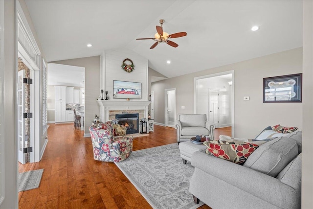 living room featuring a large fireplace, ceiling fan, light hardwood / wood-style flooring, and vaulted ceiling