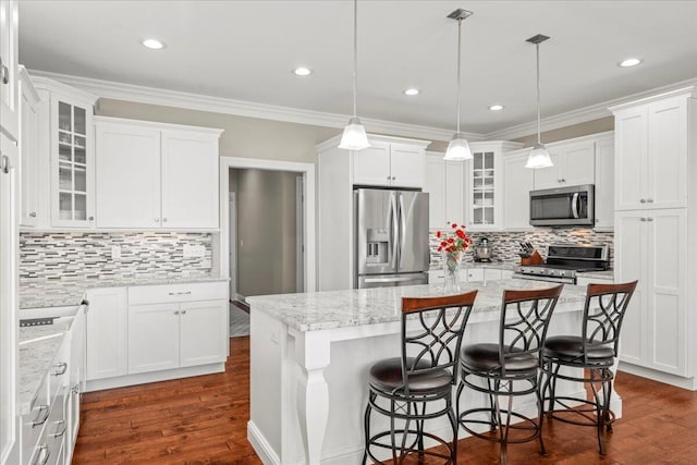 kitchen featuring ornamental molding, stainless steel appliances, pendant lighting, white cabinets, and an island with sink