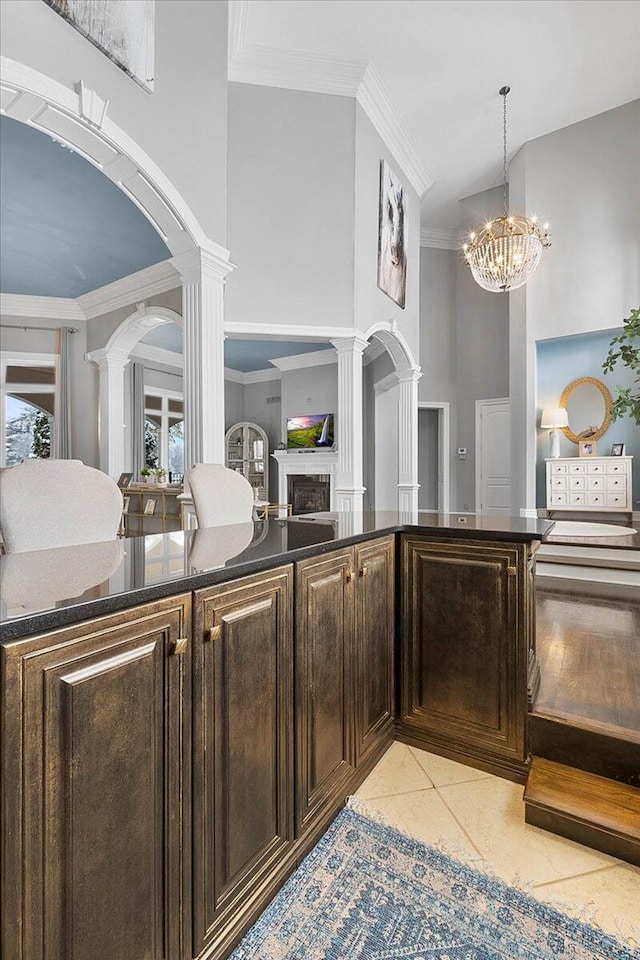 kitchen featuring an inviting chandelier, hanging light fixtures, ornate columns, light tile patterned floors, and dark brown cabinetry