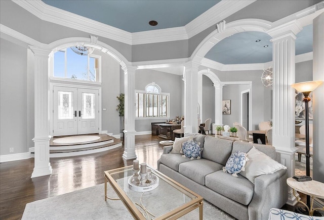 living room with decorative columns, crown molding, dark hardwood / wood-style flooring, and an inviting chandelier