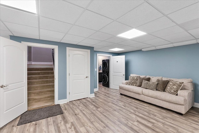 unfurnished living room featuring light hardwood / wood-style floors, a drop ceiling, and stacked washer / drying machine