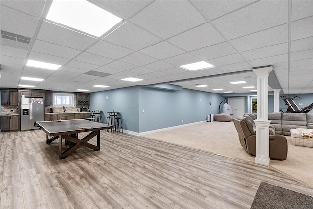 game room featuring decorative columns, a paneled ceiling, sink, and light wood-type flooring