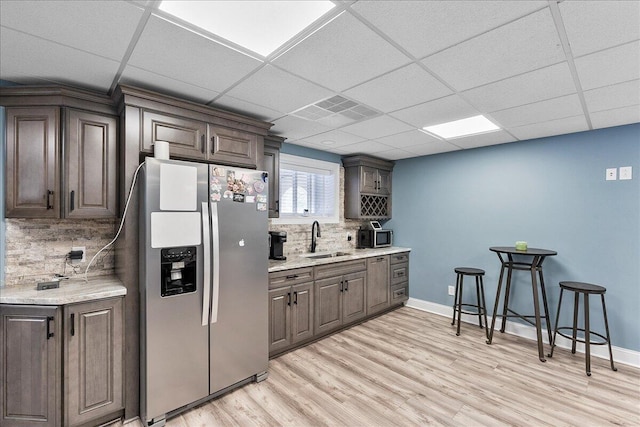 kitchen featuring decorative backsplash, a drop ceiling, dark brown cabinetry, sink, and stainless steel fridge with ice dispenser