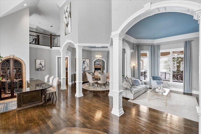 foyer entrance featuring a towering ceiling, ornate columns, ornamental molding, dark wood-type flooring, and a notable chandelier