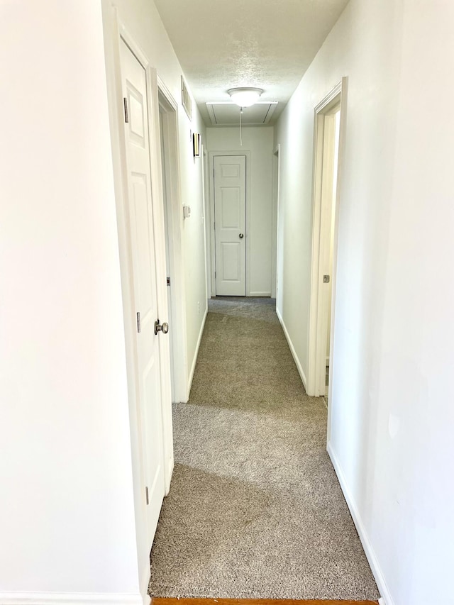 hall featuring a textured ceiling, light colored carpet, visible vents, baseboards, and attic access