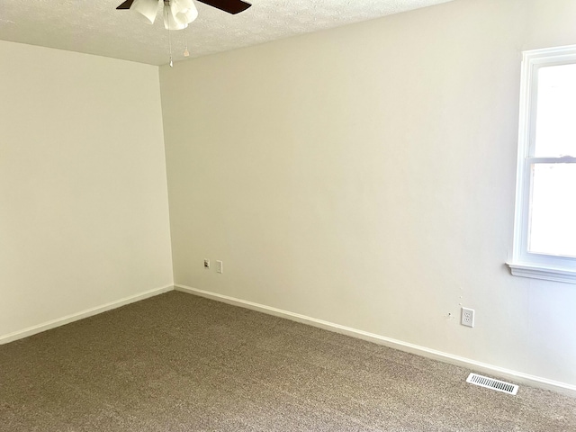 spare room with a textured ceiling, dark colored carpet, visible vents, and baseboards