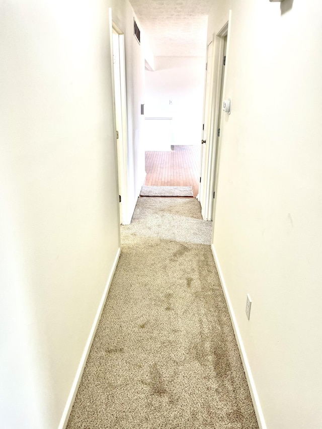 corridor featuring carpet, visible vents, a textured ceiling, and baseboards