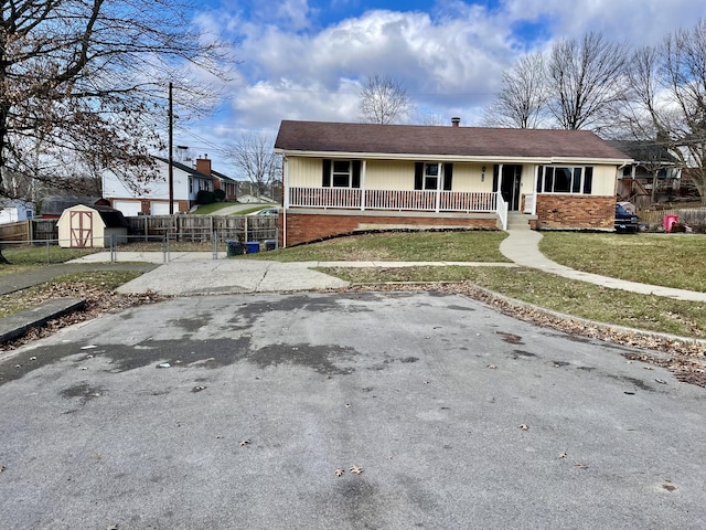 ranch-style home with brick siding, a storage unit, a porch, fence, and an outdoor structure