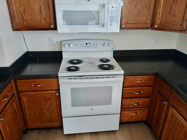 kitchen featuring dark countertops, white appliances, brown cabinetry, and wood finished floors