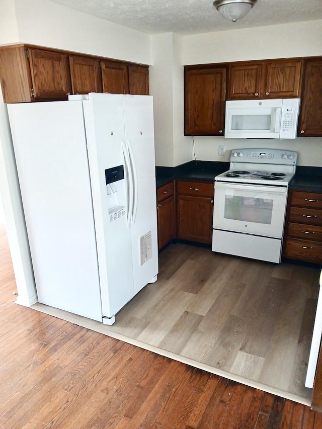 kitchen with dark countertops, white appliances, a textured ceiling, and wood finished floors