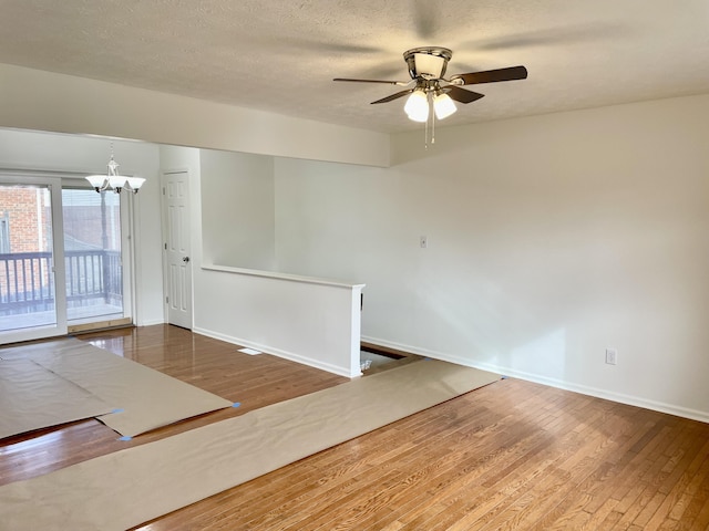 unfurnished room featuring a textured ceiling, baseboards, wood finished floors, and ceiling fan with notable chandelier