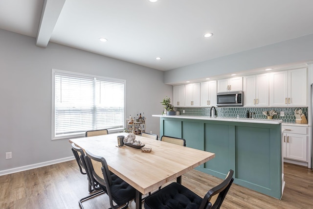 dining room featuring beamed ceiling, light wood-type flooring, and sink